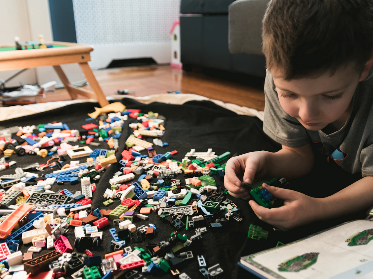 A school-age boy building with LEGO bricks from an idea book